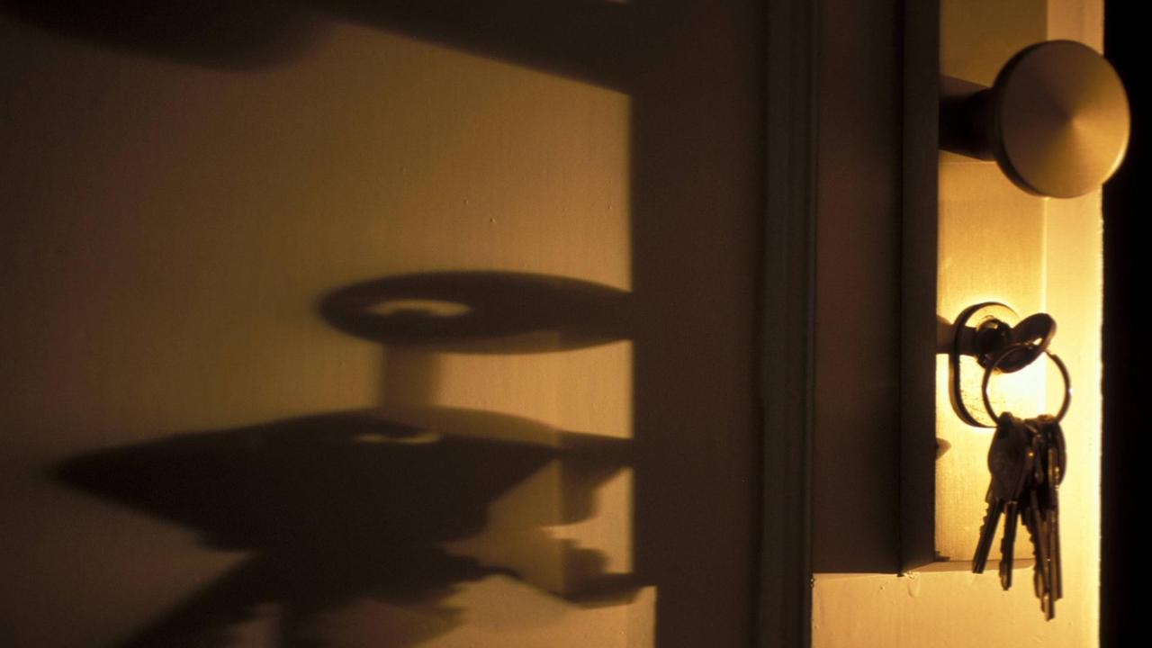 Ein Schlüssel steckt im Schloss einer Tür. Seitlich einfallendes Licht erzeugt unheimliche Schatten. Ein Schlüssel steckt im Schloss einer Tür. Seitlich einfallendes Licht erzeugt unheimliche Schatten.