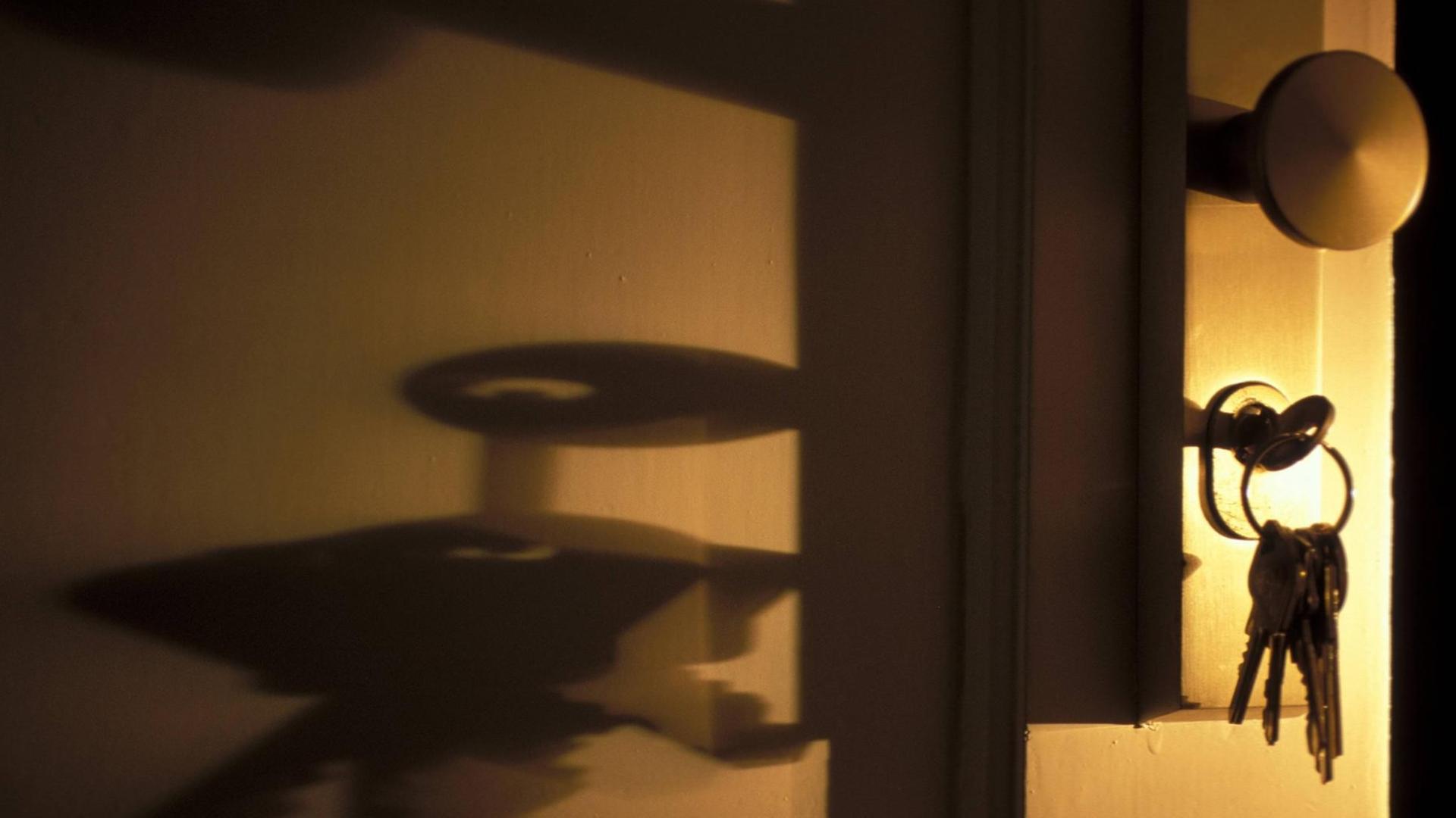 Ein Schlüssel steckt im Schloss einer Tür. Seitlich einfallendes Licht erzeugt unheimliche Schatten. Ein Schlüssel steckt im Schloss einer Tür. Seitlich einfallendes Licht erzeugt unheimliche Schatten.