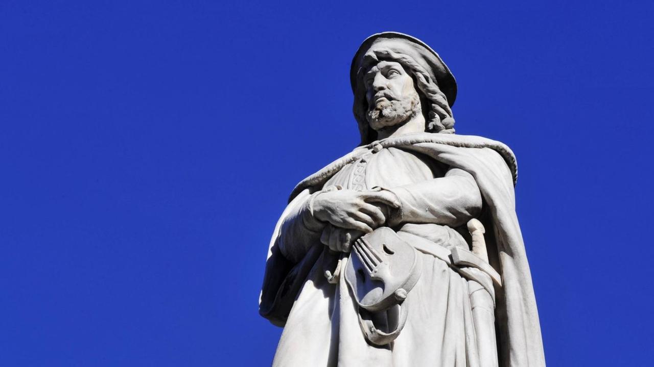 Eine idealisierte Mamorstatue hebt sich vom strahlend blauen Himmel ab. Der Mann mit krausem Haar hält ein Saiteninstrument fest.