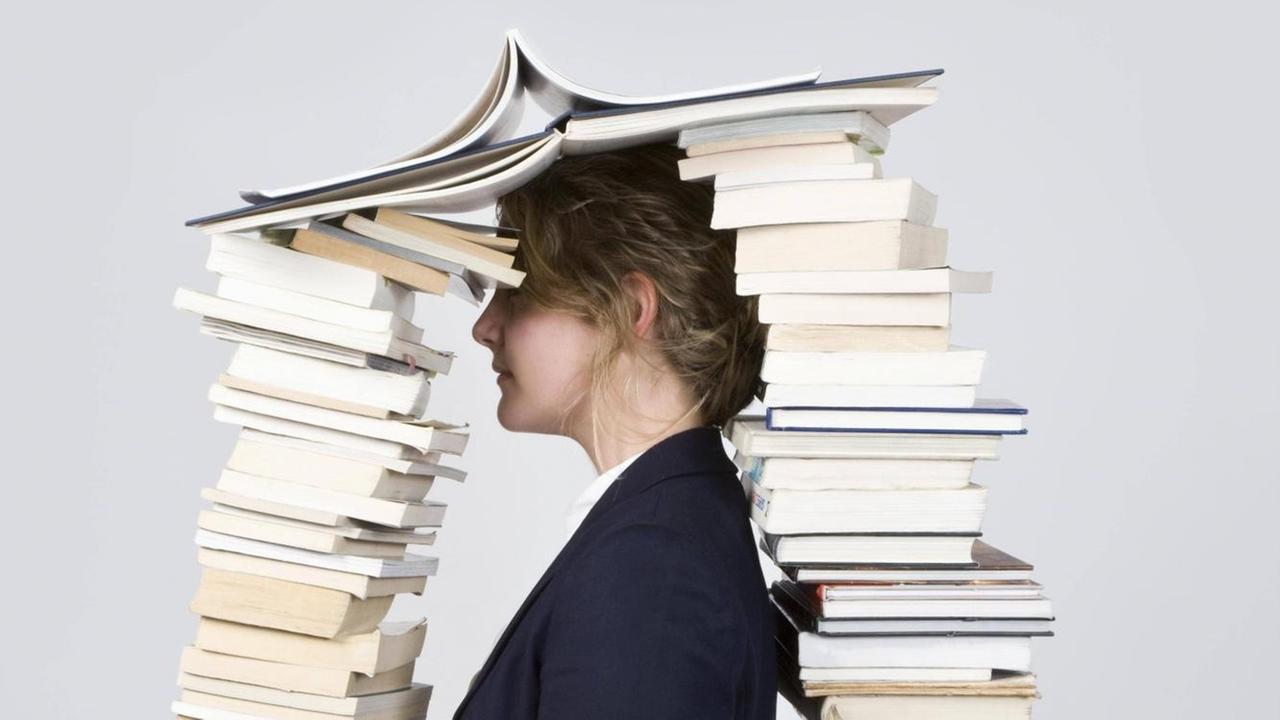 Eine Frau mit dem Kopf zwischen zwei hohen Bücherstapeln. Eine Frau mit dem Kopf zwischen zwei hohen Bücherstapeln.