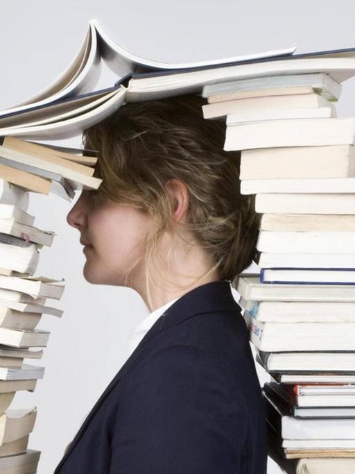 Eine Frau mit dem Kopf zwischen zwei hohen Bücherstapeln.