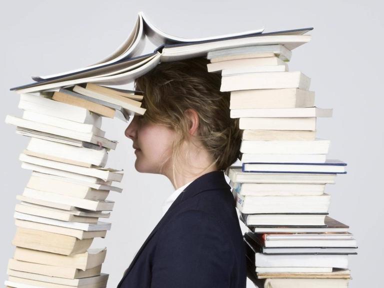 Eine Frau mit dem Kopf zwischen zwei hohen Bücherstapeln.