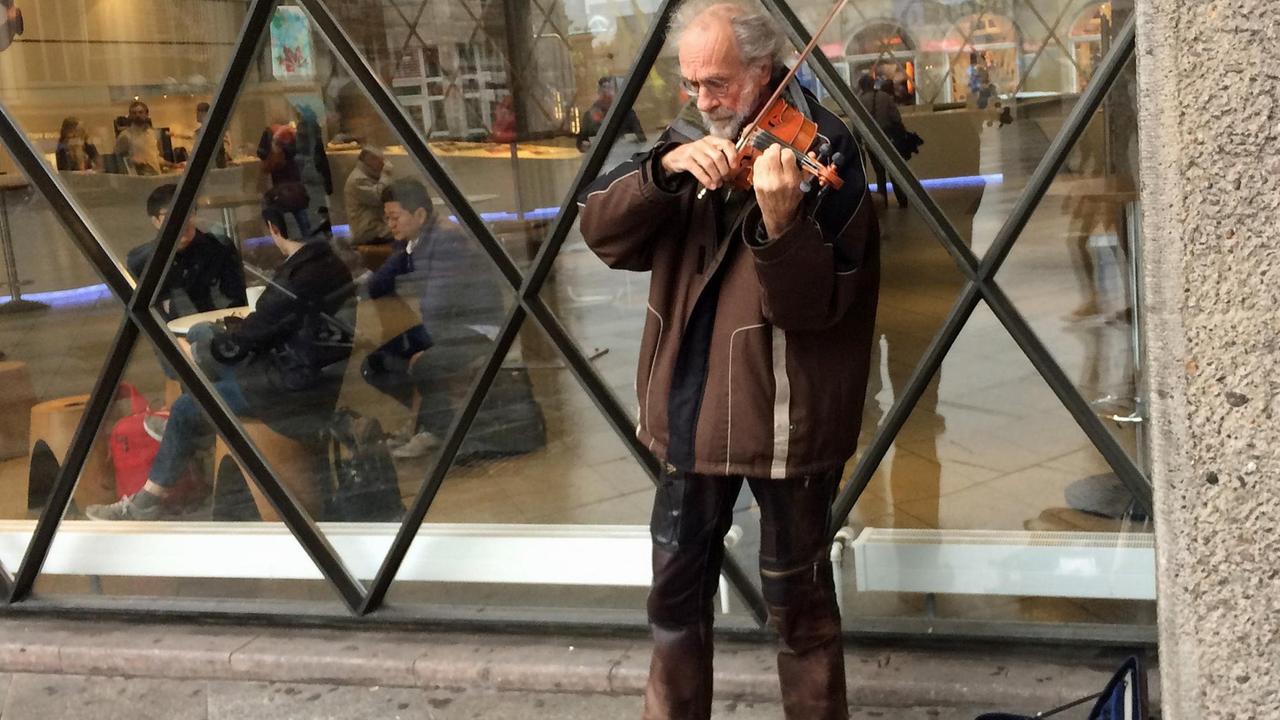 Der Straßenmusiker Klaus Wrochem spielt auf seiner Geige vor einem Schaufenster auf der Kölner Domplatte. Der Straßenmusiker Klaus Wrochem spielt auf seiner Geige vor einem Schaufenster auf der Kölner Domplatte.