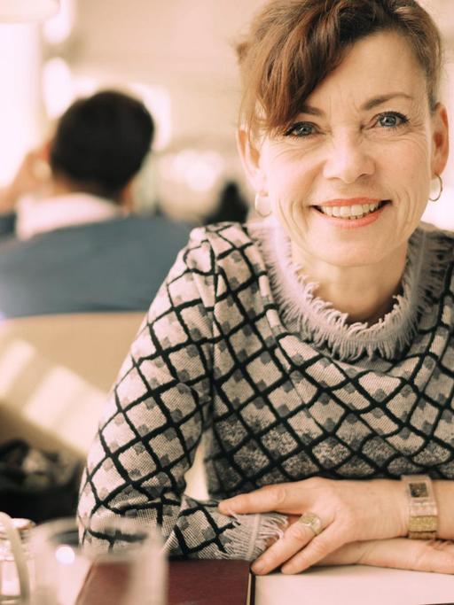 Renata Schmidtkunz sitzt in einem Cafe und lächelt in die Kamera.