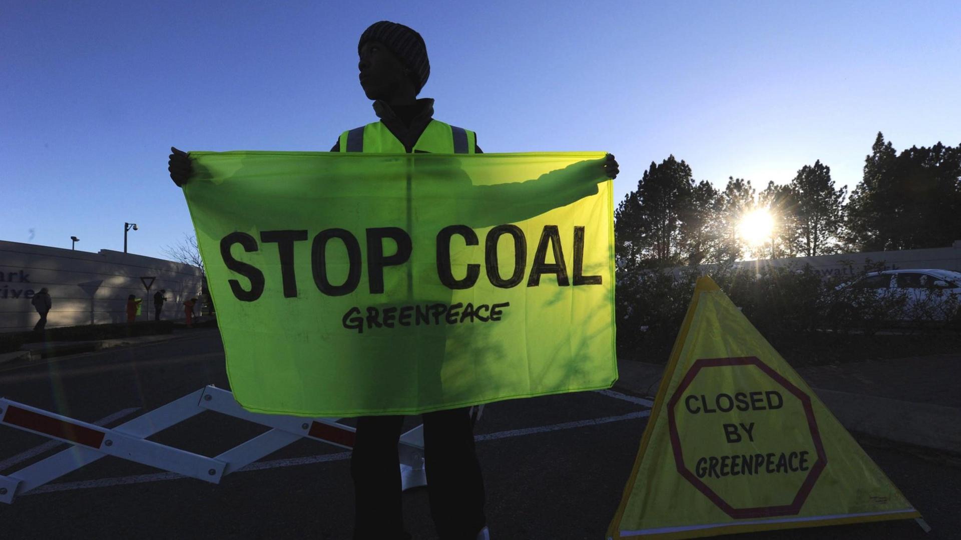 Ein südafrikanischer Greenpeace-Aktivist hält ein Flagge mit der Aufschrift "Stop Coal" in Händen.
