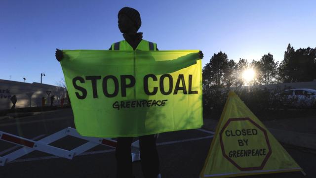 Ein südafrikanischer Greenpeace-Aktivist hält ein Flagge mit der Aufschrift "Stop Coal" in Händen.