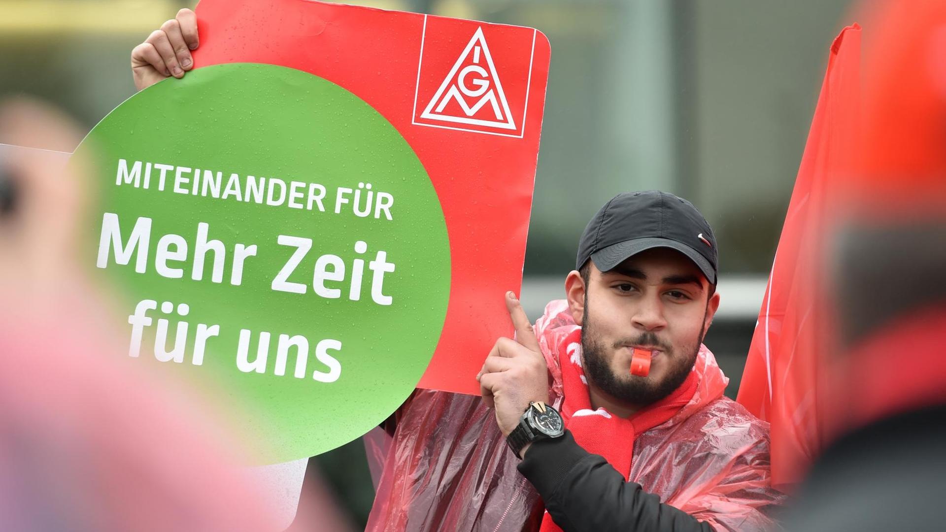 Miteinander für mehr Zeit für uns, steht auf einem Plakat der IG Metall, das ein Mann bei einer Kundgebung hoch hält. Miteinander für mehr Zeit für uns, steht auf einem Plakat der IG Metall, das ein Mann bei einer Kundgebung hoch hält.
