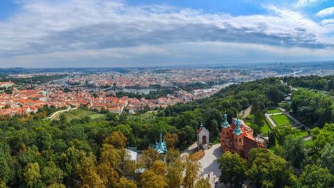 Blick über einen grünen Hügel zur Stadt Prag, die von der Moldau durchzogen wird.