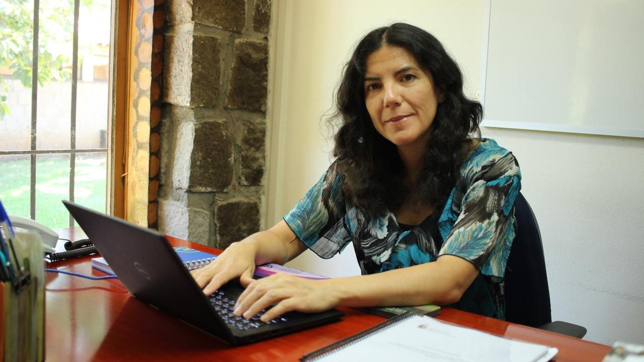 María Muñoz sitzt an ihrem Schreibtisch und schaut freundlich in die Kamera. María Muñoz sitzt an ihrem Schreibtisch und schaut freundlich in die Kamera.