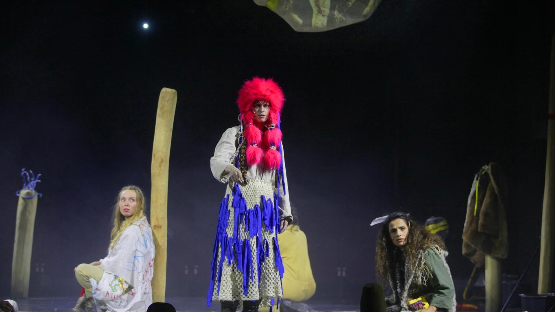 Szenenausschnitt mit Riah Knight, Lea Draeger, Sesede Terziyan aus "Rewitching Europe" von Yael Ronen. Die Schauspielerinnen sind auf eine kargen Bühne zu sehen, auf der es nur ein paar verteilte Holzstäbe zu sehen gibt. Szenenausschnitt mit Riah Knight, Lea Draeger, Sesede Terziyan aus "Rewitching Europe" von Yael Ronen. Die Schauspielerinnen sind auf eine kargen Bühne zu sehen, auf der es nur ein paar verteilte Holzstäbe zu sehen gibt.