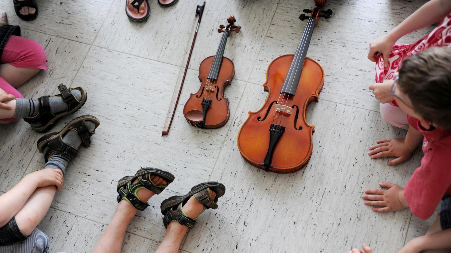 In der Musikschule. Kinder sitzen um zwei Streichinstrumente herum. In der Musikschule. Kinder sitzen um zwei Streichinstrumente herum.