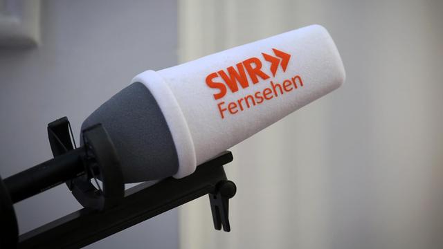 Man sieht ein Mikrofon mit einem weißen Windschutz, auf dem in roten Buchstaben "SWR Fernsehen" steht.