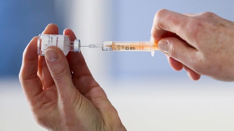 Frauen-Hände ziehen eine Spritze mit einer Impf-Dosis auf.