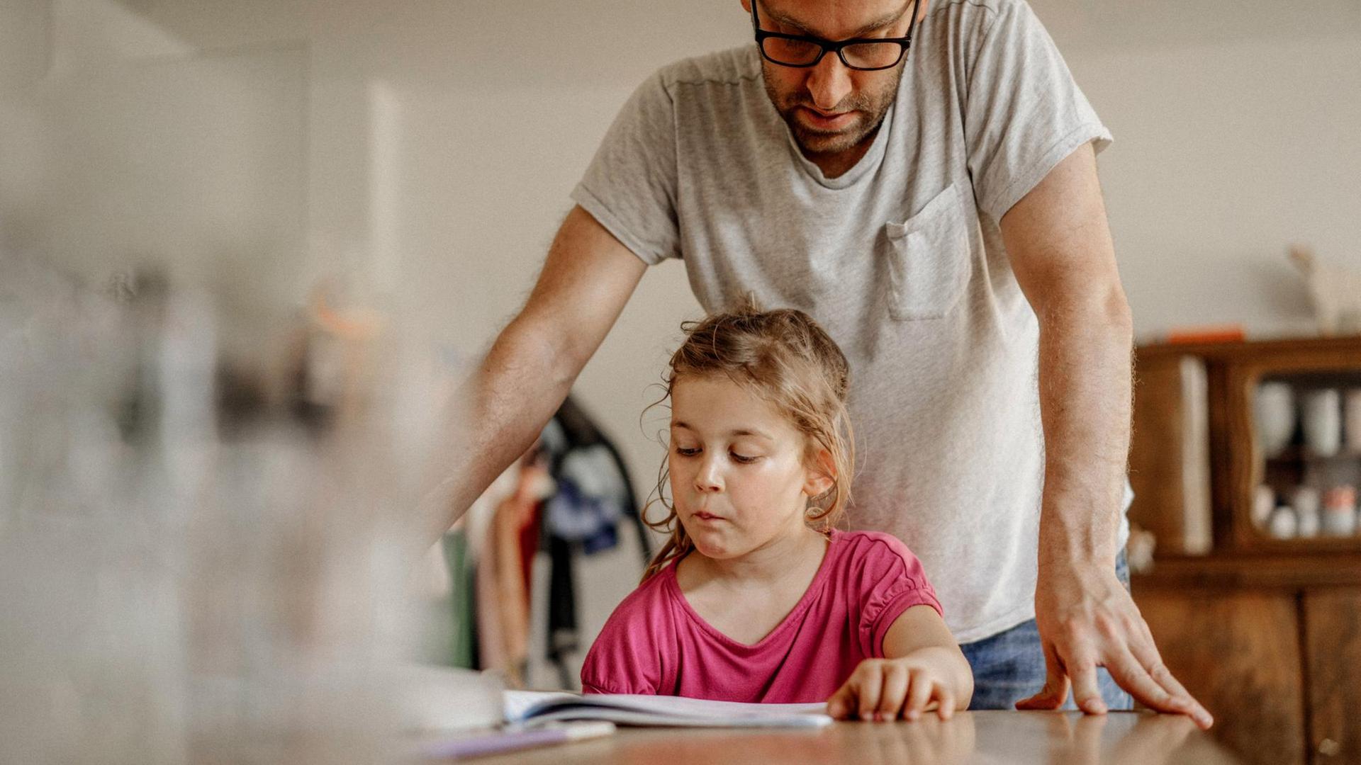 Ein Vater schaut über die Schulter seiner Tochter auf ihre Hausaufgaben