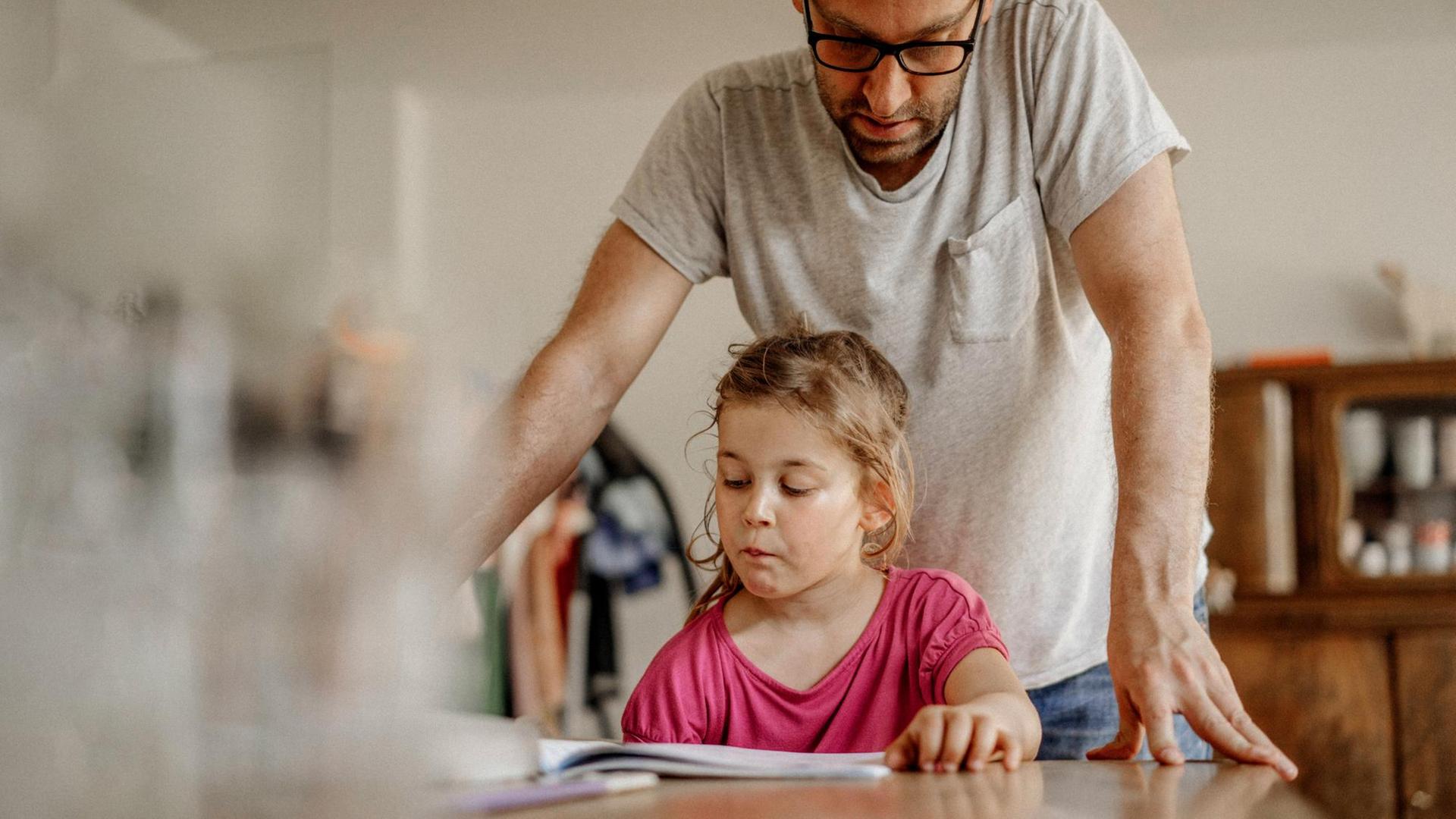 Ein Vater schaut über die Schulter seiner Tochter auf ihre Hausaufgaben Ein Vater schaut über die Schulter seiner Tochter auf ihre Hausaufgaben