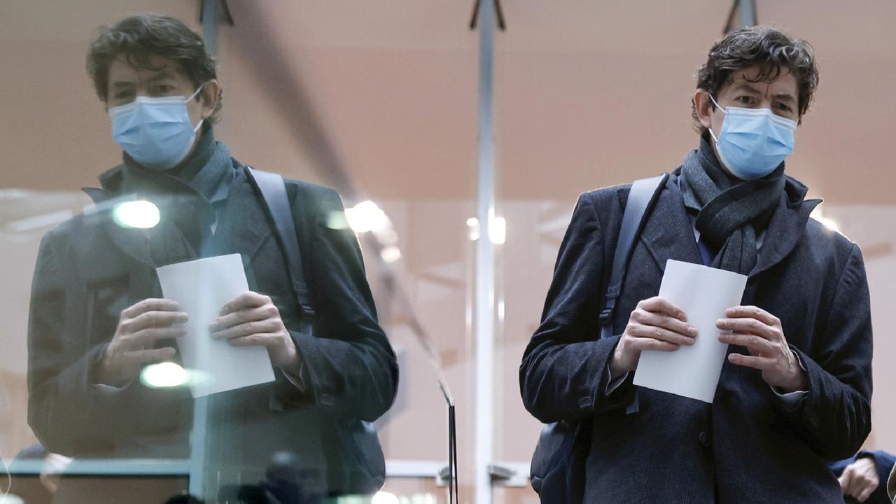 Virologe Christian Drosten mit Schutzmaske über Mund und Nase verlässt eine Pressekonferenz in Berlin. Links daneben ist ein zweiter Christian Drosten zu sehen - als Spiegelbild in einer Glasscheibe.