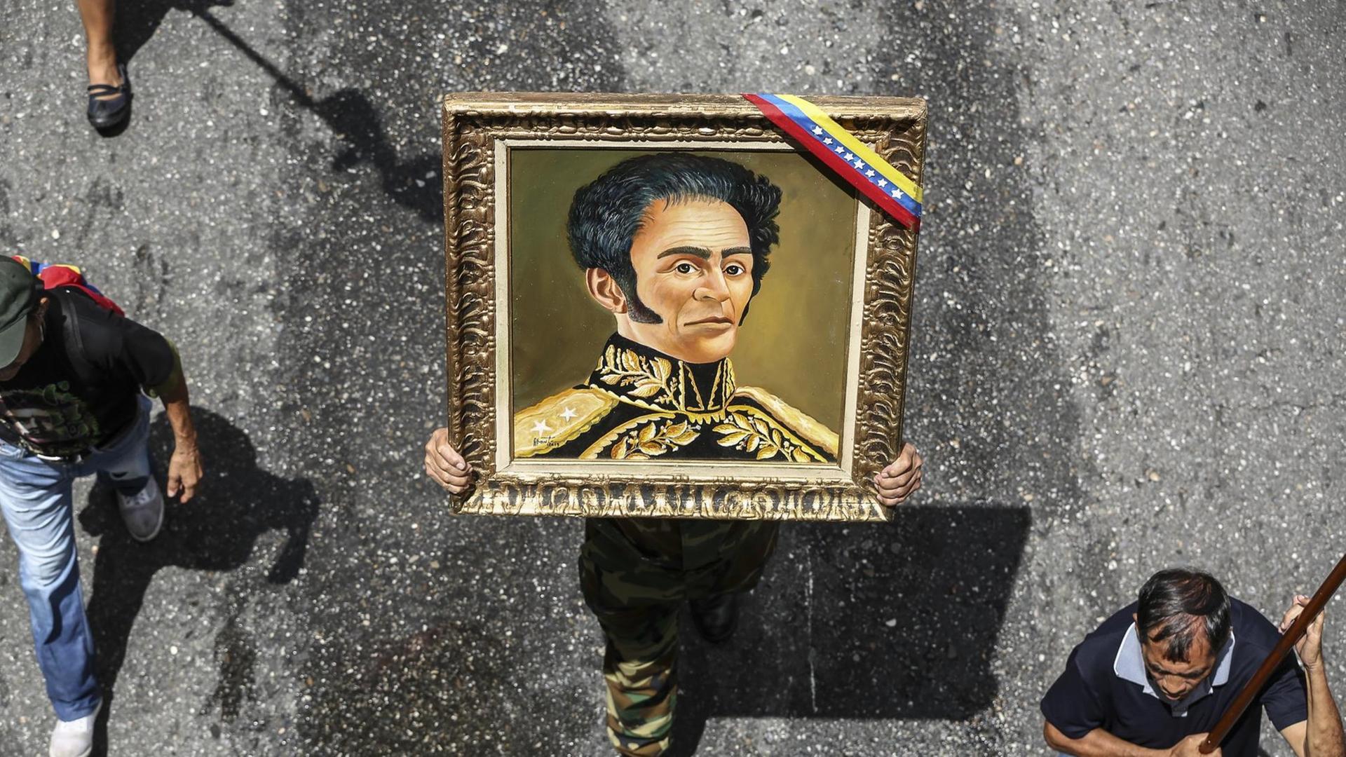 Venezuela, Caracas: Ein Mann hält während einer Demonstration ein Gemälde von Simon Bolivar. Die Menschen demonstrieren gegen den jüngsten Bericht der Vereinten Nationen über die Menschenrechtslage in dem südamerikanischen Land.