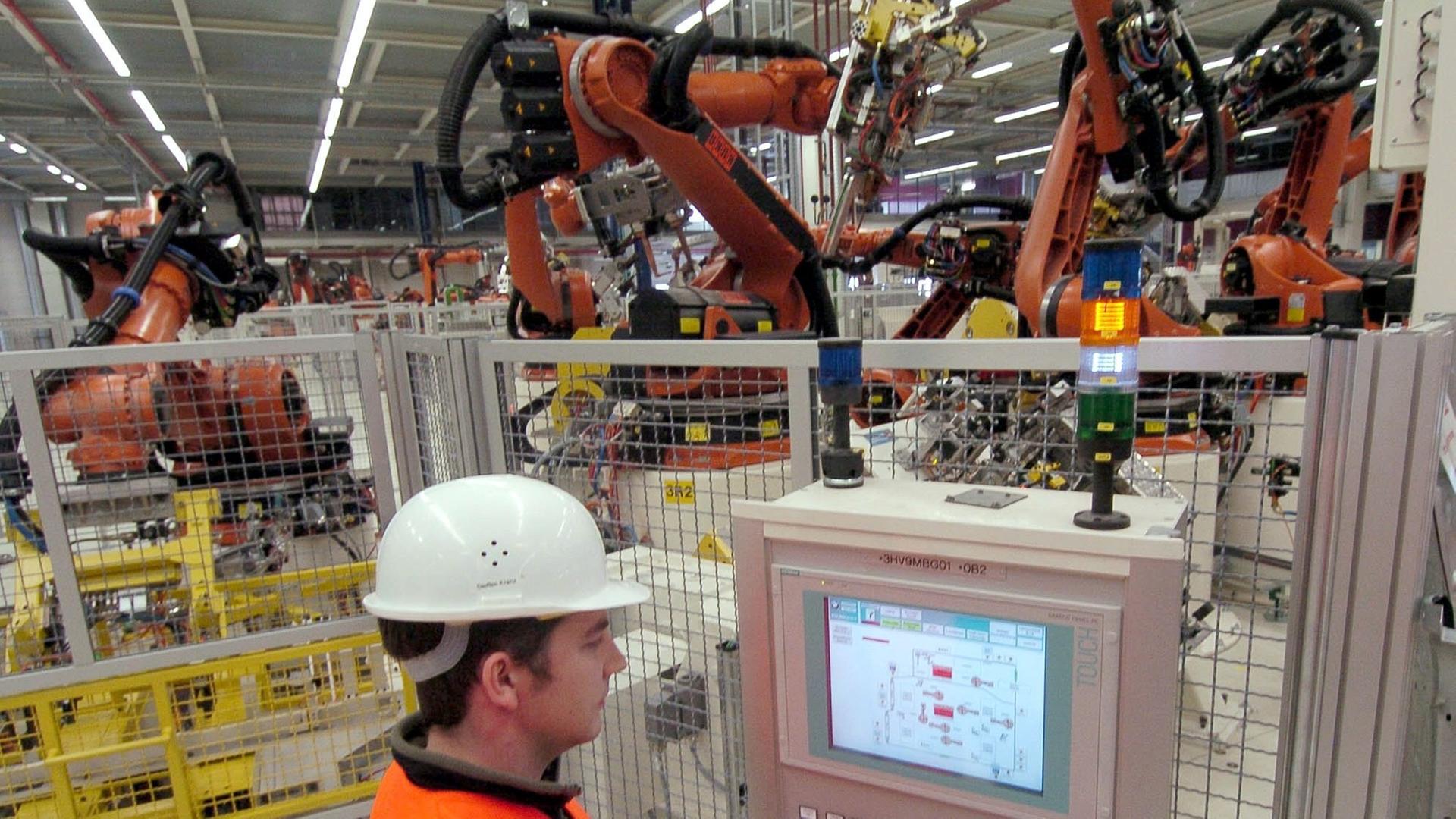 Ein Mitarbeiter arbeitet in der Karosseriebauhalle des BMW-Werkes Leipzig. Die herkömmlichen Roboter im Hintergrund sind durch ein Schutzgitter von den Arbeitern getrennt
