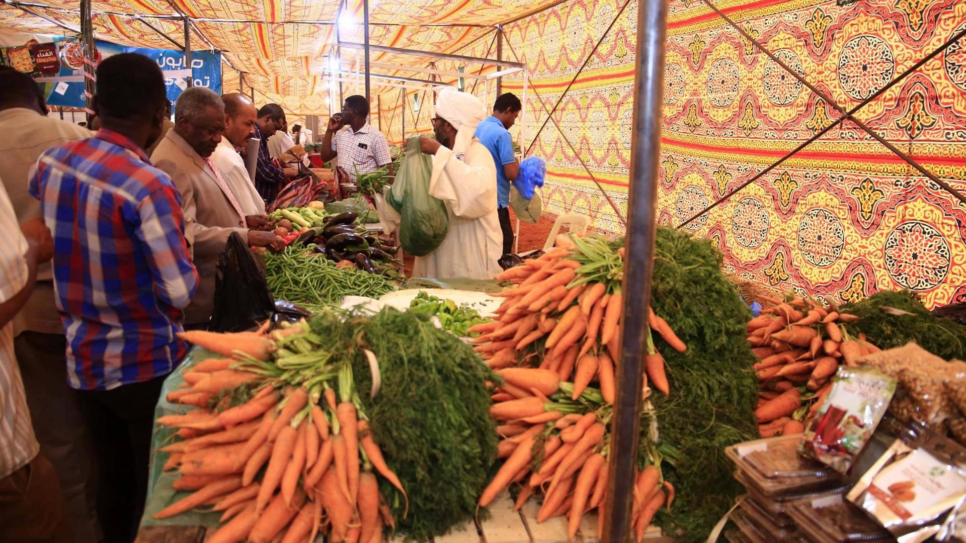 Ein Marktzelt in der sudanesischen Hauptstadt Khartoum . Ein Bauer verkauft an einem Tisch Möhren und anderes Gemüse. Ein Marktzelt in der sudanesischen Hauptstadt Khartoum . Ein Bauer verkauft an einem Tisch Möhren und anderes Gemüse.
