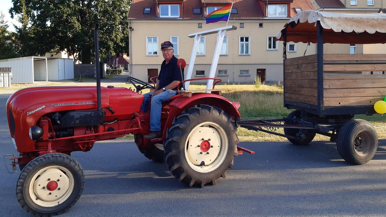 Ein Landwirt fährt auf seinem roten Traktor, der mit einer Regenbogenfahne geschmückt ist Ein Landwirt fährt auf seinem roten Traktor, der mit einer Regenbogenfahne geschmückt ist