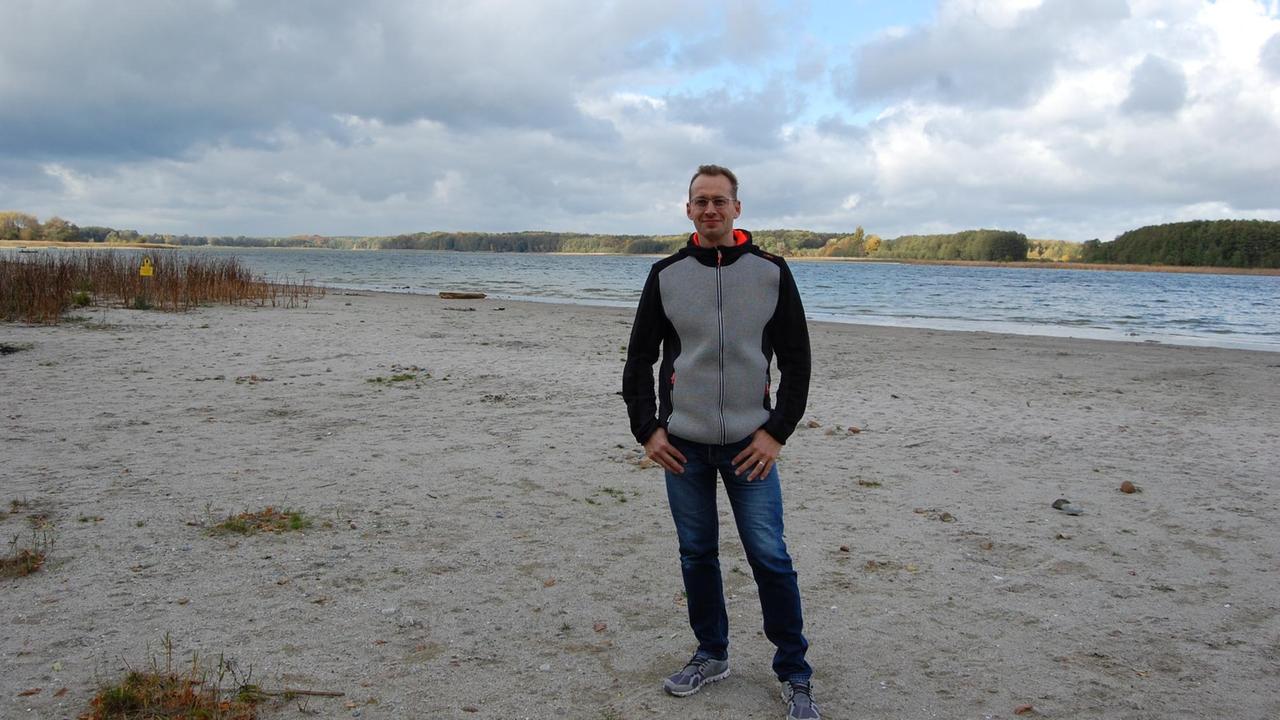 Jürgen Wagler steht am Ufer des Seddiner Sees auf einem sandigen Strand.