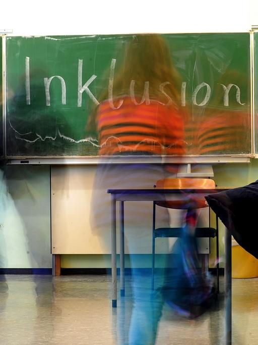 Ein Schulkind steht vor einer Tafel, auf der das Wort "Inklusion" geschrieben steht.