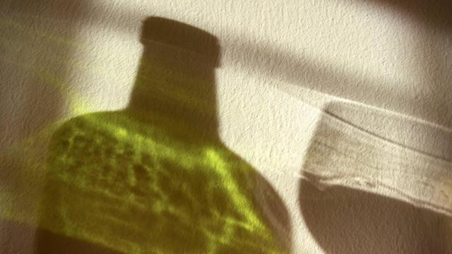 Der Schatten einer Rotweinflasche und eines Rotweinglases auf einer Wand.