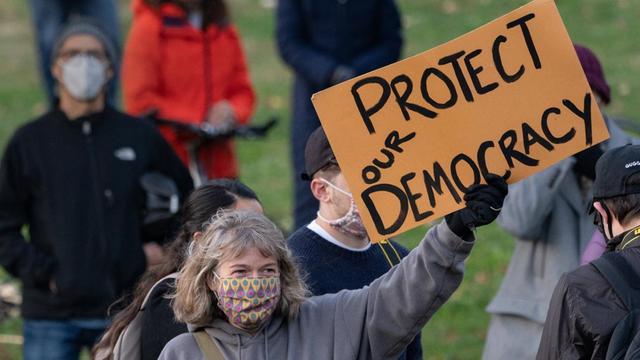 Eine Demonstrantin hält ein Schild mit der Aufschrift "Protect our democracy" ("Beschützt unsere Demokratie").