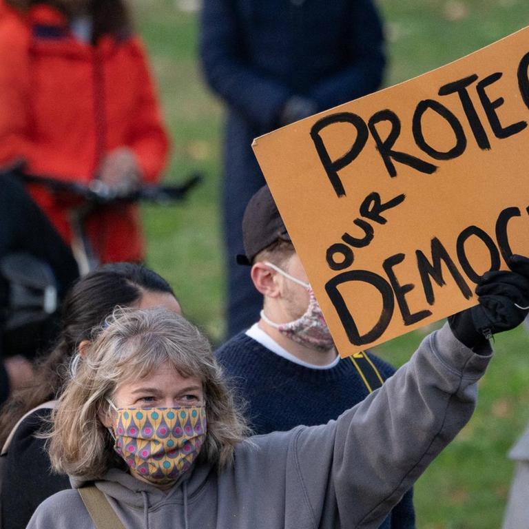 Eine Demonstrantin hält ein Schild mit der Aufschrift "Protect our democracy" ("Beschützt unsere Demokratie").