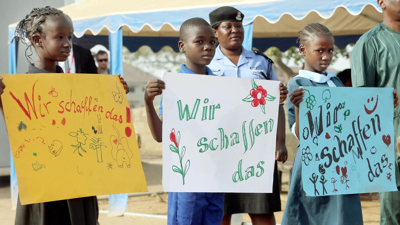 Kinder halten in Abuja in Nigeria, im Lager für Binnenflüchtlinge New Kuchigoro, selbst gemalte Schilder mit der Aufschrift "Wir schaffen das" hoch, bevor der Bundespräsident kommt. 