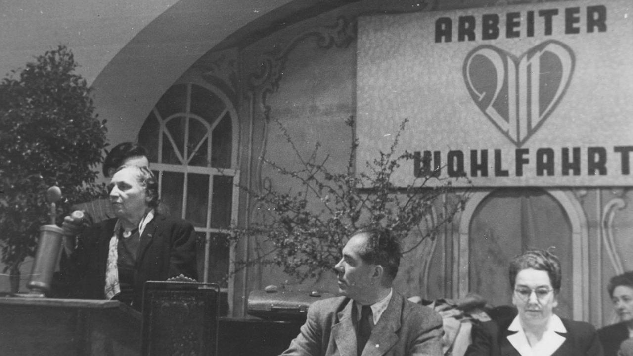 AWO-Gründerin Marie Juchacz (l), Franz Neumann und Ida Wolff Ende der 40er-Jahre auf einer Veranstaltung der Arbeiterwohlfahrt. Eine Frau steht an einem Rednerpult, daneben sitzen ein Mann und eine Frau. AWO-Gründerin Marie Juchacz (l), Franz Neumann und Ida Wolff Ende der 40er-Jahre auf einer Veranstaltung der Arbeiterwohlfahrt. Eine Frau steht an einem Rednerpult, daneben sitzen ein Mann und eine Frau.