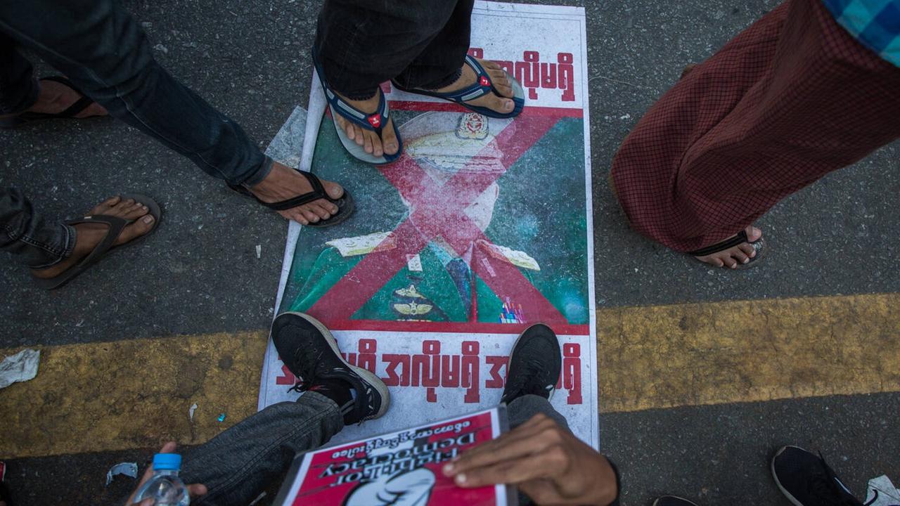 Diverse Füße von Demonstranten treten auf ein Plakat mit dem Konterfei General Min Aung Hlaing in der Nähe des Rathauses von Rangoon im Februar 2021. Diverse Füße von Demonstranten treten auf ein Plakat mit dem Konterfei General Min Aung Hlaing in der Nähe des Rathauses von Rangoon im Februar 2021.