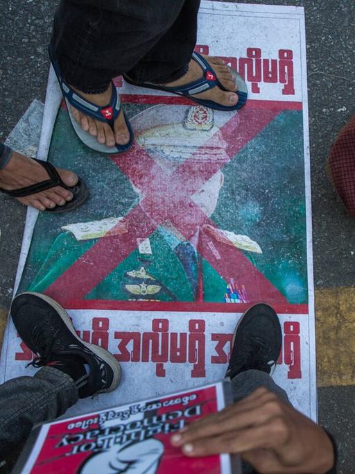 Diverse Füße von Demonstranten treten auf ein Plakat mit dem Konterfei General Min Aung Hlaing in der Nähe des Rathauses von Rangoon im Februar 2021.
