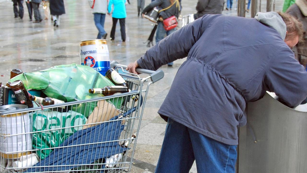 Ein Mann sucht in einem Mülleimer nach Pfandflaschen.