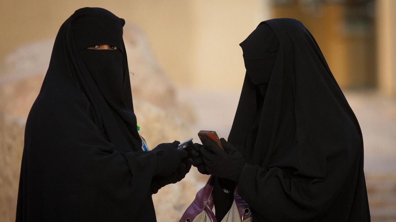 Zwei Frauen, voll verschleiert mit der traditonellen Abaya, tippen in Riad in Saudi-Arabien auf ihren Handys.