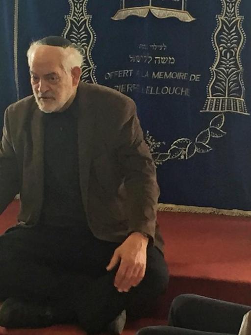 Der Rabbiner Michel Serfaty sitzt in der Synagoge auf einer Stufe und spricht mit muslimischen Jugendlichen
