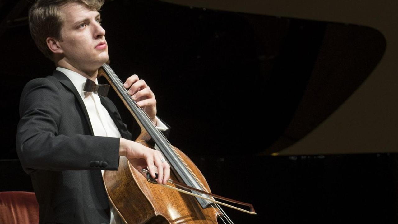 Ein junger Mann sitzt auf einer Bühne und spielt Violoncello. Ein junger Mann sitzt auf einer Bühne und spielt Violoncello.