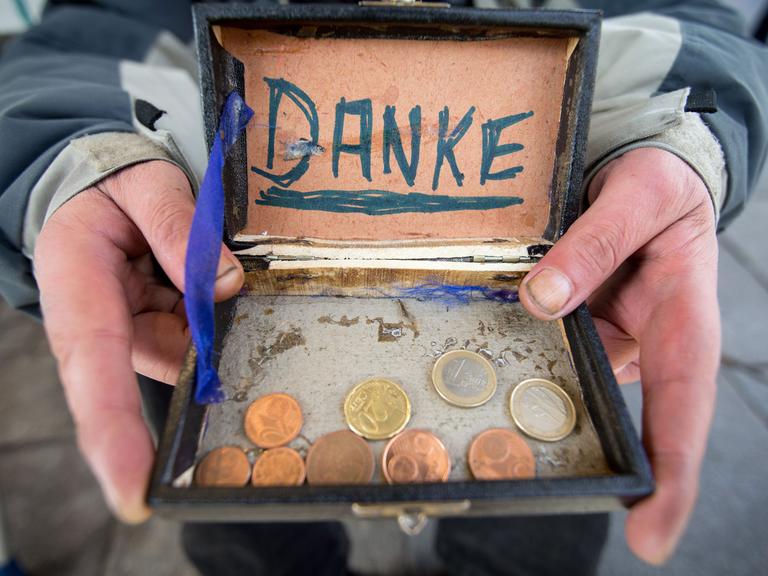 Ein Bettler hält eine alte Zigarrenkiste für Geldspenden in der Hand.