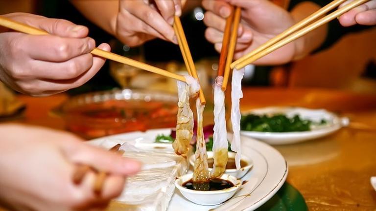 Mehrere Hände mit Stäbchen essen die japanische Fischspezialität Kugelfisch auch als Fugu bekannt. Mehrere Hände mit Stäbchen essen die japanische Fischspezialität Kugelfisch auch als Fugu bekannt.