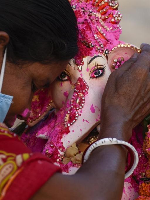 Eine Frau in traditionell hinduistischer Kleidung betet an einer Ganesha Figur.