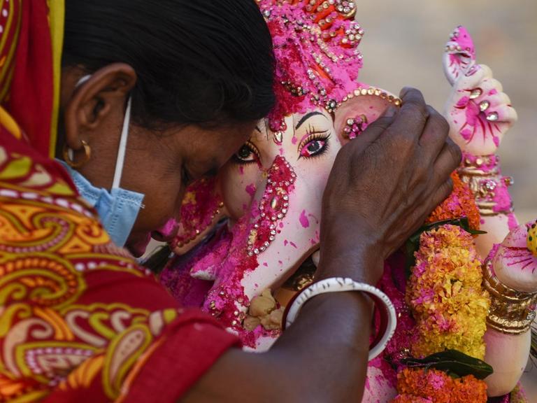 Eine Frau in traditionell hinduistischer Kleidung betet an einer Ganesha Figur.