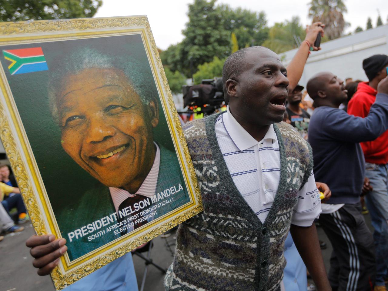 Ein Mann hält ein Portraitfoto des verstorbenen Nelson Mandela. Ein Mann hält ein Portraitfoto des verstorbenen Nelson Mandela.