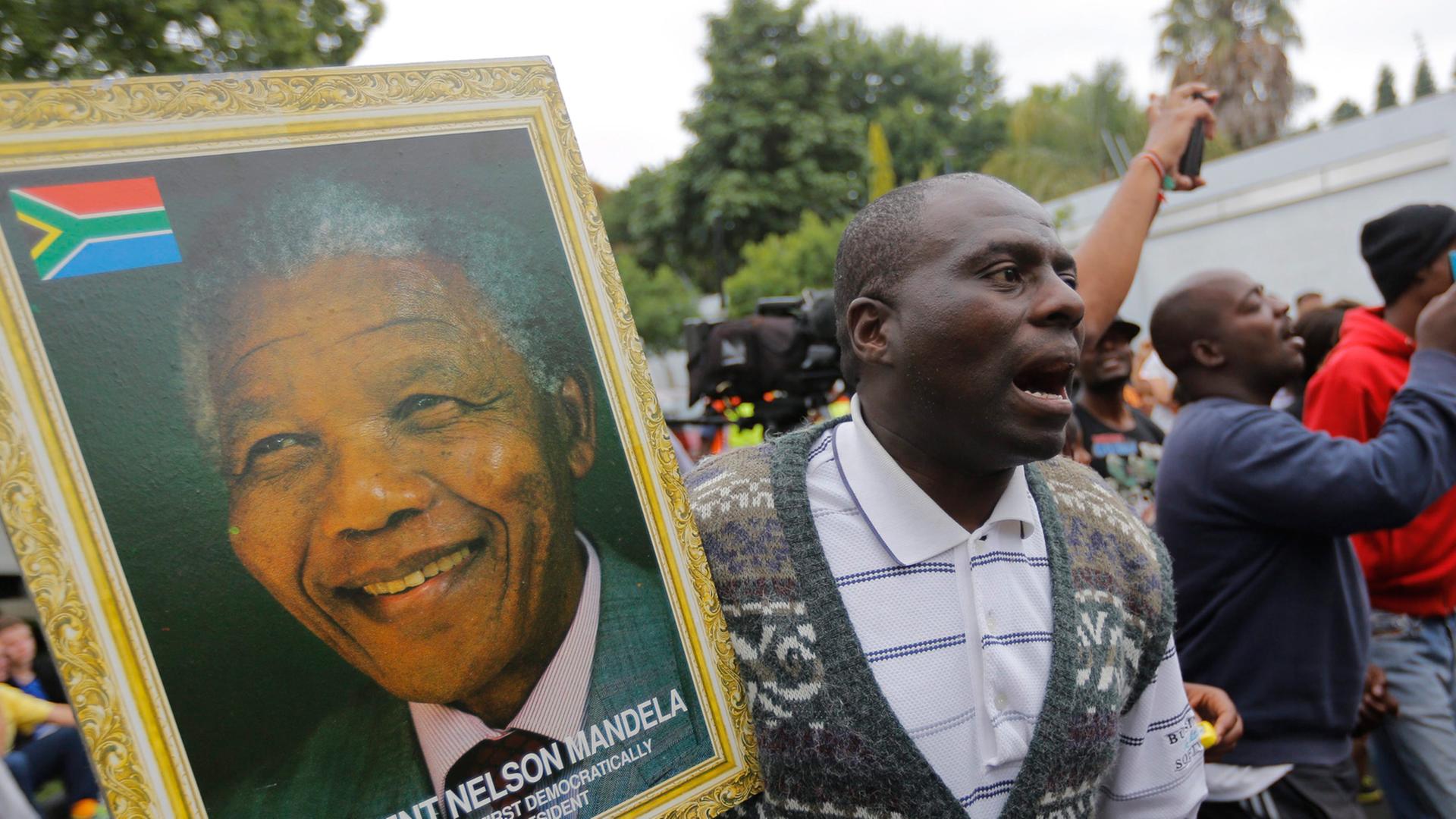 Ein Mann hält ein Portraitfoto des verstorbenen Nelson Mandela. Ein Mann hält ein Portraitfoto des verstorbenen Nelson Mandela.