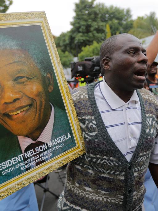 Ein Mann hält ein Portraitfoto des verstorbenen Nelson Mandela.