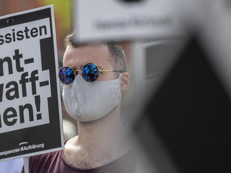 Ein Mann verfolgt eine Ansprache bei der offiziellen Gedenkveranstaltung zu den rassistisch motivierten Anschlägen in Hanau. Dabei hält er ein Schild mit der Aufschrift «Rassisten entwaffnen» in der Hand. Unter dem Motto «Erinnerung - Gerechtigkeit - Aufklärung - Konsequenzen» versammelten sich die Teilnehmer auf einem Platz in der Innenstadt. Aufgrund der aktuellen Corona-Infektionszahlen war die Teilnehmerzahl von der Behörden begrenzt worden.