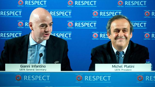Infantino und Platini sitzen bei einer pressekonferenz und lächeln.