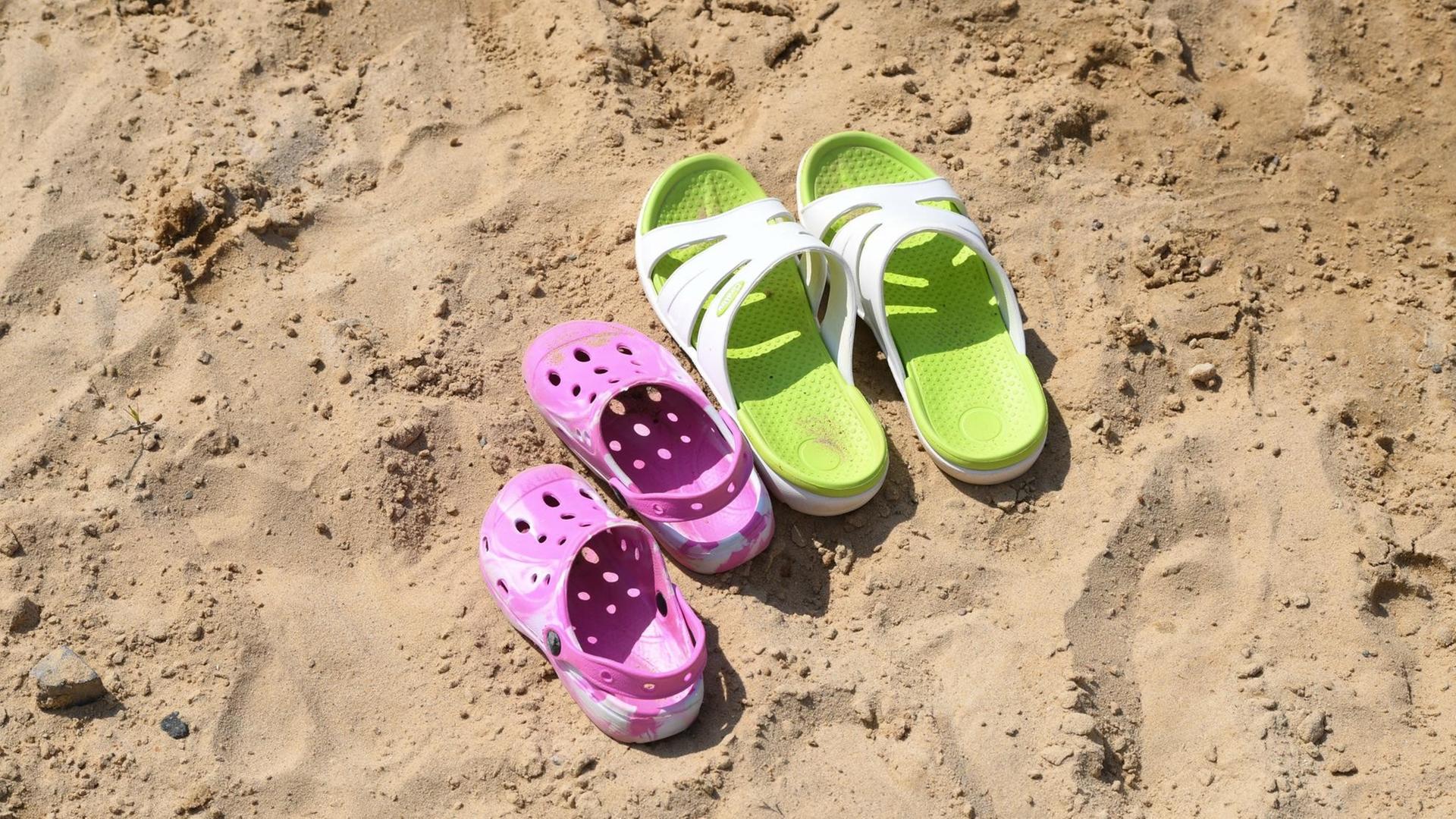 Zwei Paar Badeschuhe stehen auf dem Sand. Zwei Paar Badeschuhe stehen auf dem Sand.