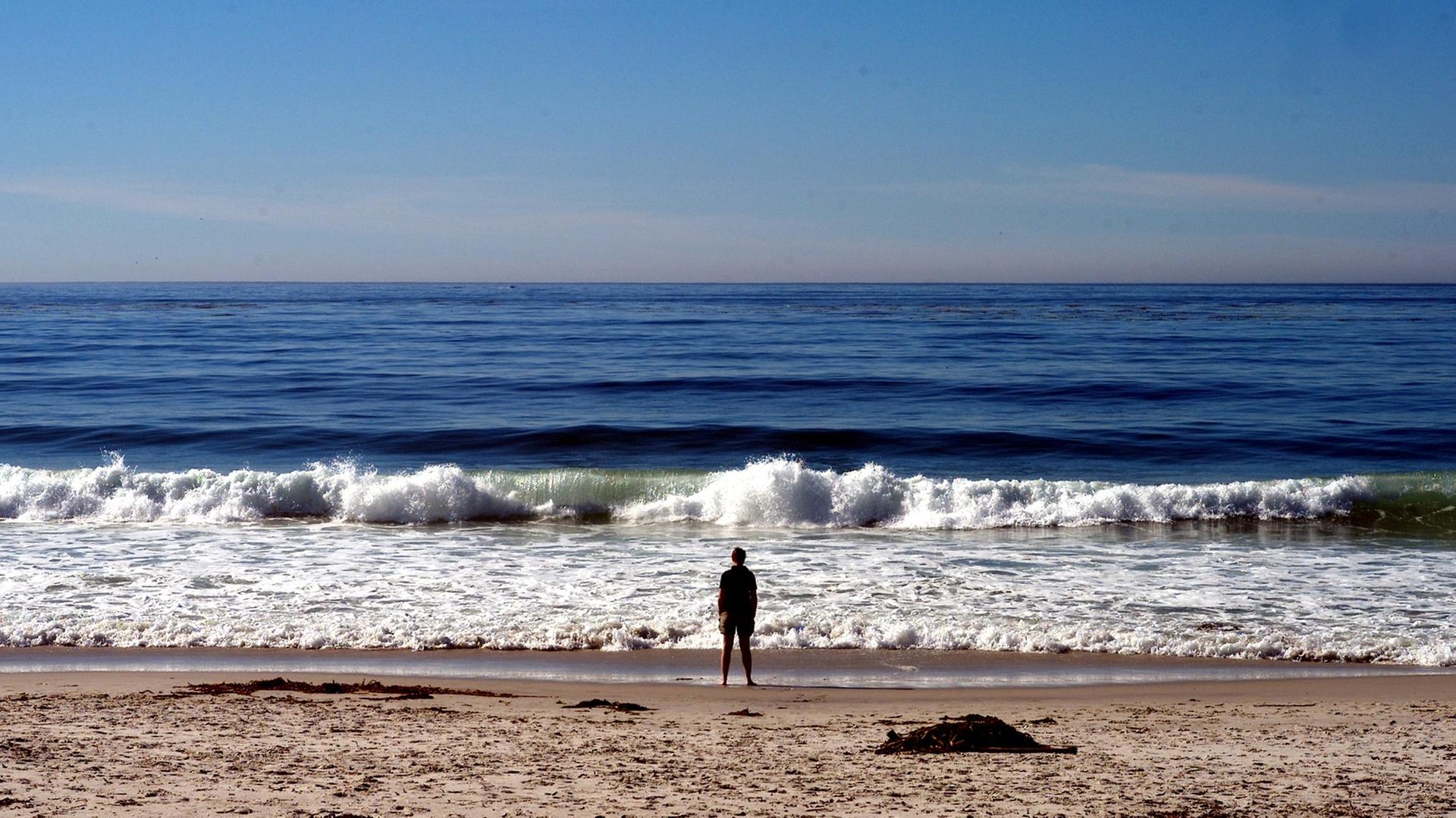 Eine Mann steht am Pazifikstrand von Carmel in Kalifornien und blickt aufs Meer