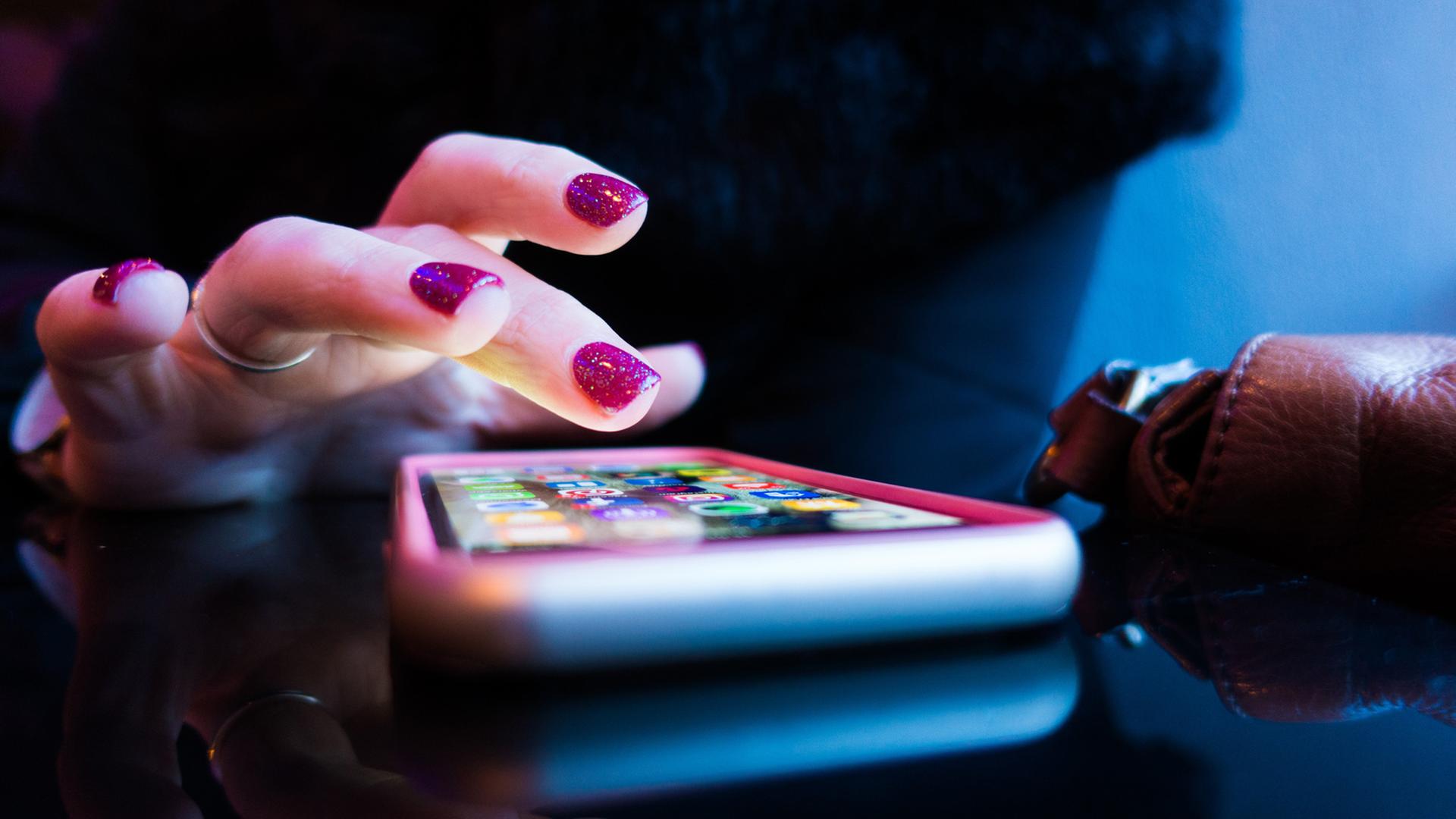 Ein Frauenhand mit violett lackierten Fingernägeln tippt auf ein Smartphone. Ein Frauenhand mit violett lackierten Fingernägeln tippt auf ein Smartphone.