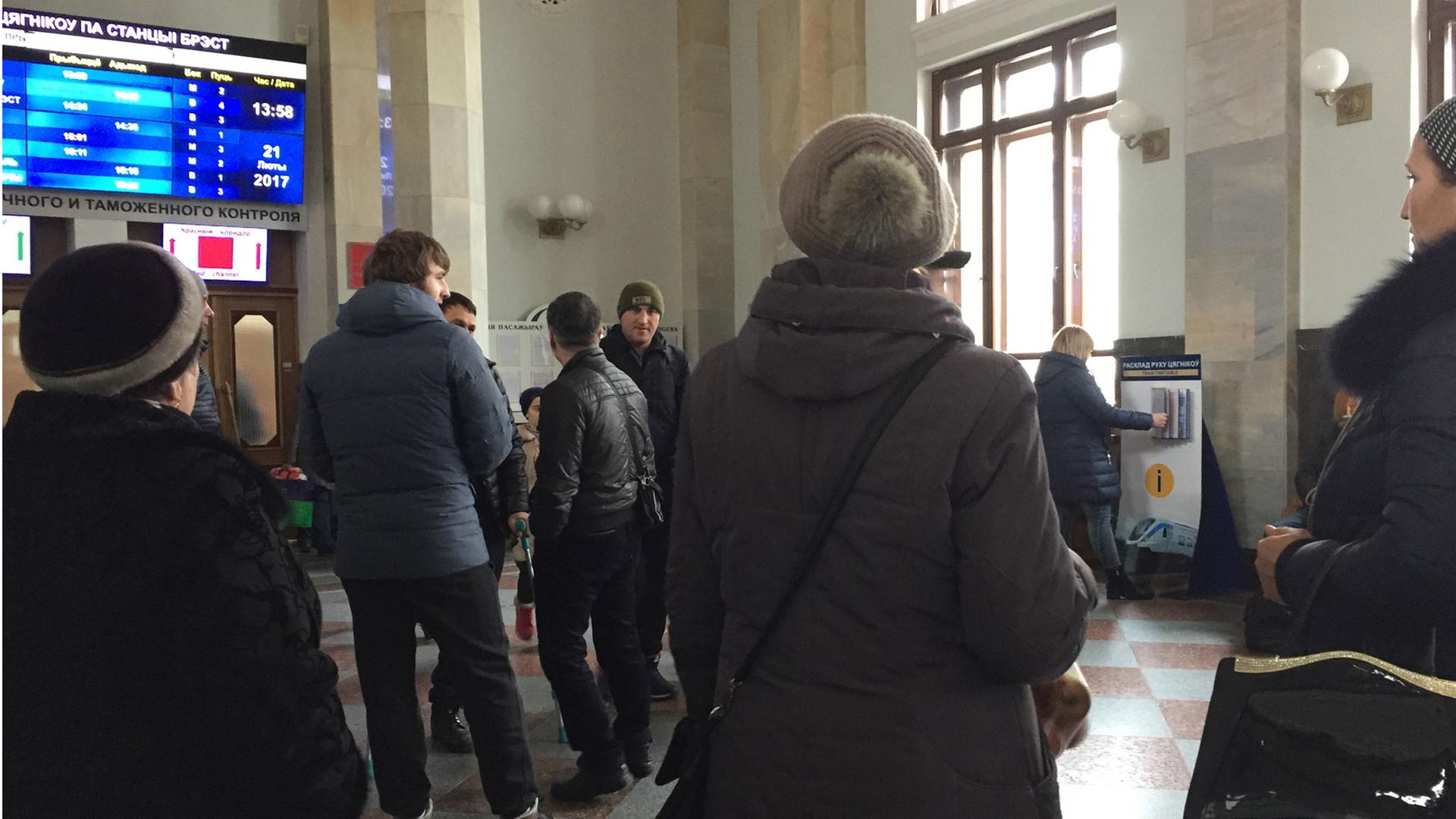 Das Bild zeigt wartende Tschetschenen am Bahnhof von Brest von hinten. Sie schauen auf eine Anzeigetafel im Bahnhof. Von dort aus versuchen viele Menschen, über Polen in die Europäische Union zu gelangen. Das Bild zeigt wartende Tschetschenen am Bahnhof von Brest von hinten. Sie schauen auf eine Anzeigetafel im Bahnhof. Von dort aus versuchen viele Menschen, über Polen in die Europäische Union zu gelangen.